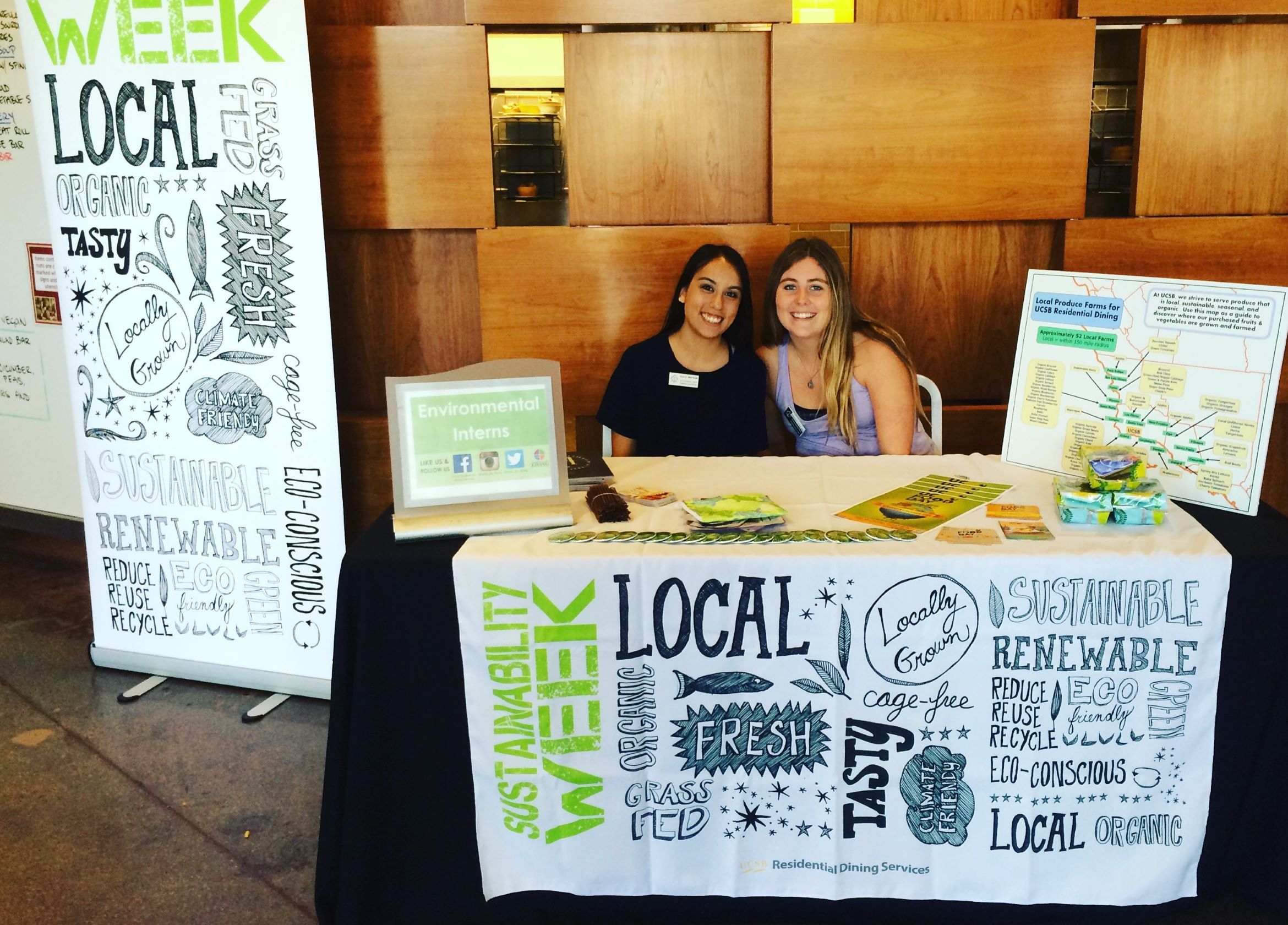 two Interns sitting at a table in front of DLG with information about sustainability